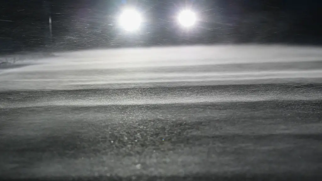 Die-Scheinwerfer-eines-Autos-scheinen-ueber-eine-verschneite-Strasse