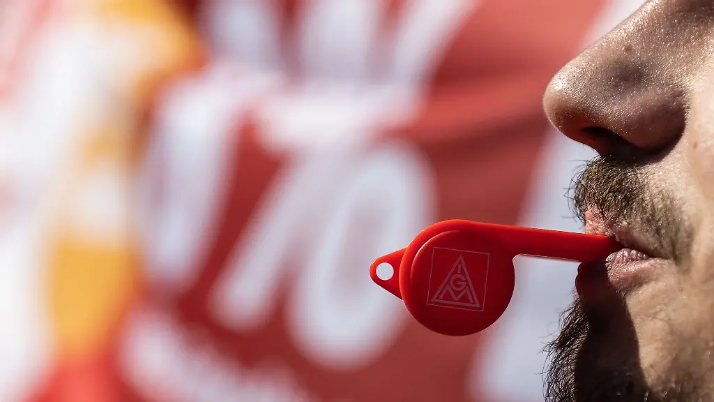 Ein-Beschaeftigter-pustet-bei-einem-Warnstreik-der-IG-Metall-in-eine-Trillerpfeife