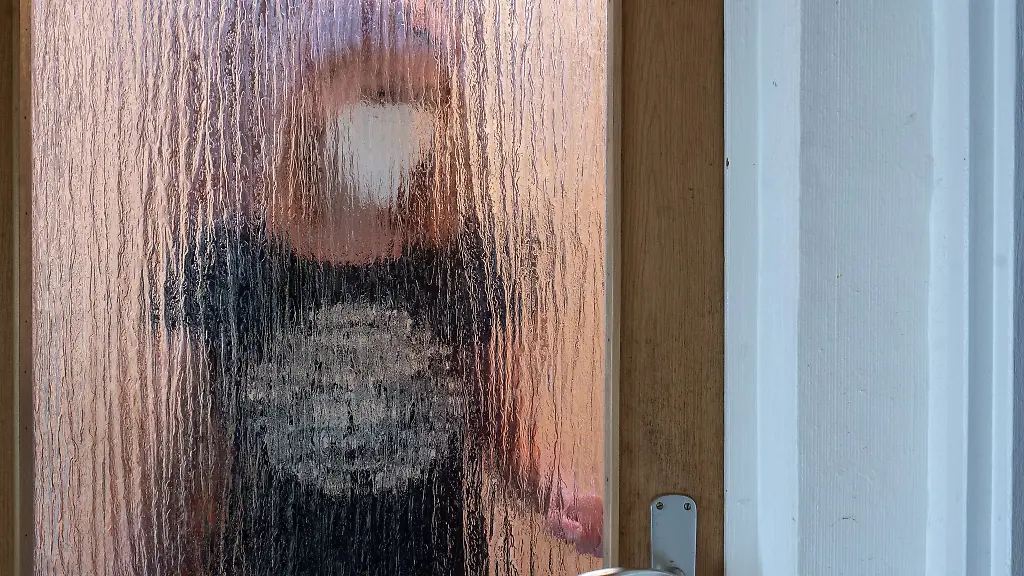 Eine-Frau-steht-waehrend-der-Isolation-nach-einem-positiven-PCR-Test-hinter-einer-Glastuer