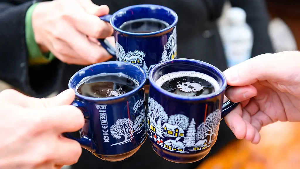 Drei-Besucher-des-Weihnachtsmarkts-stossen-mit-Gluehwein-an