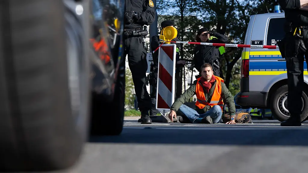Polizeibeamte-stehen-neben-einem-Klimaaktivisten-der-sich-in-der-Muenchner-Innenstadt-auf-die-Fahrbahn-geklebt-hat