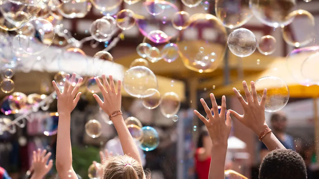 Zwei-Kinder-versuchen-im-Wind-aufsteigenden-Seifenblasen-zu-beruehren