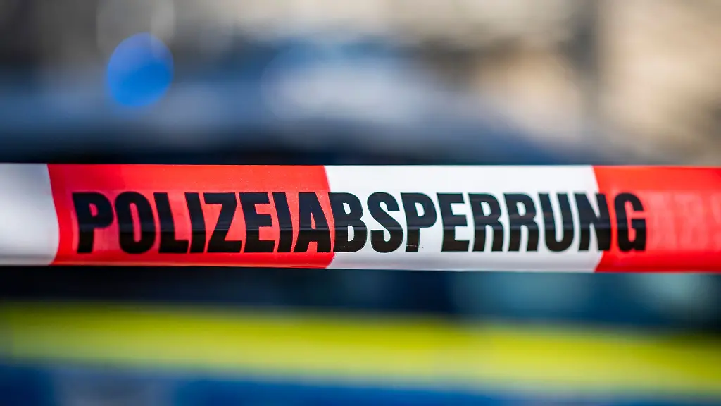 Ein-Absperrband-mit-der-Aufschrift-Polizeiabsperrung-ist-vor-einem-Polizeiwagen-aufgespannt