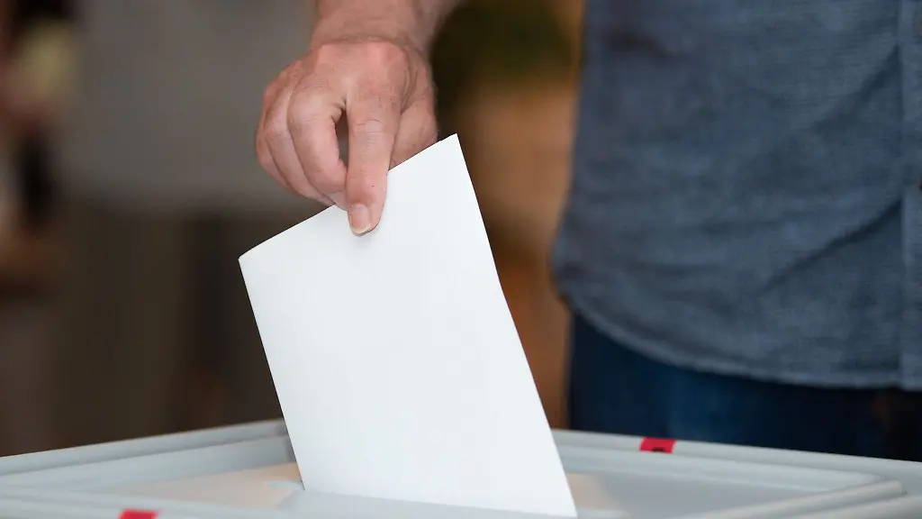 Ein-Waehler-wirft-in-einem-Wahllokal-seinen-Stimmzettel-in-die-Wahlurne
