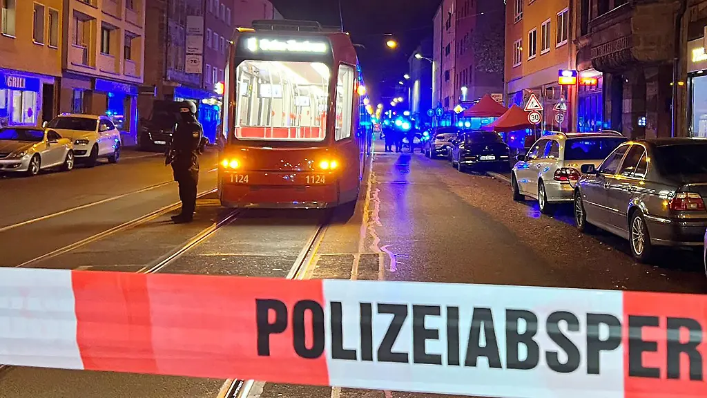 Ein-Polizist-steht-mit-einer-Maschinenpistole-neben-einer-Strassenbahn-hinter-einer-Polizeiabsperrung