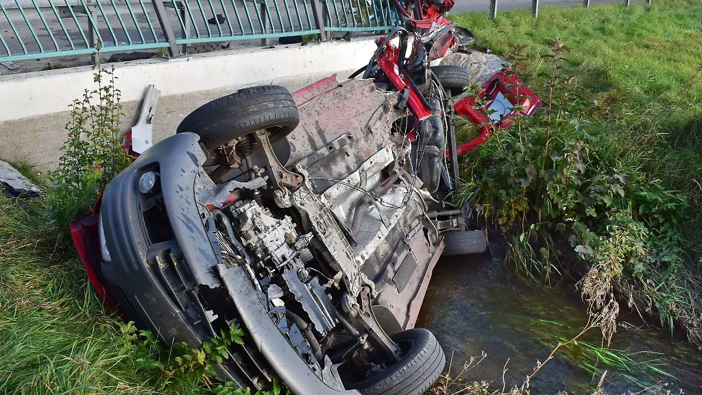 Ein-Auto-liegt-unterhalb-eines-Brueckengelaenders-in-einem-Gewaesser