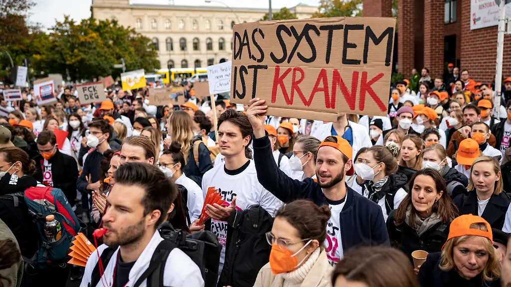 Aerzte-stehen-bei-einem-eintaegigen-Warnstreik-des-Marburger-Bunds-an-der-Charite-mit-einem-Schild-mit-der-Aufschrift-Das-System-ist-krank