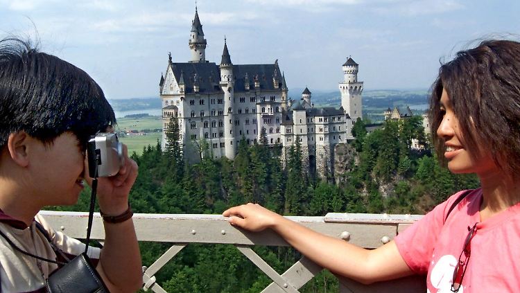 Asiatische Touristen fotografieren sich vor der Kulisse des Schlosses Neuschwanstein.