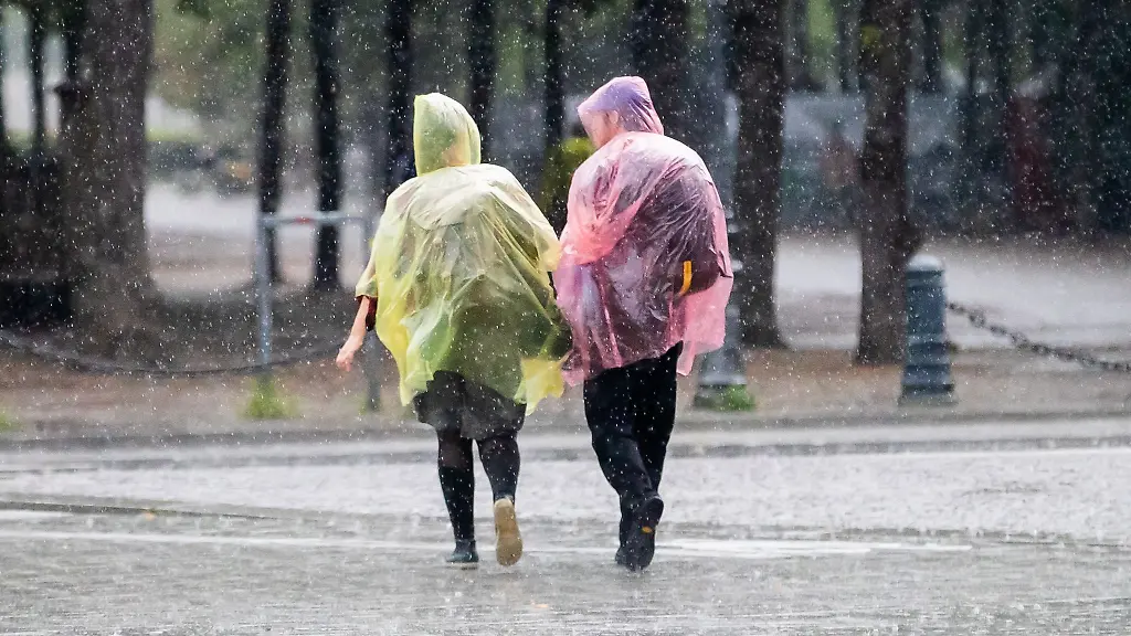 Passanten-mit-Regenmaenteln-aus-Plastik-gehen-bei-Regen-ueber-die-Strasse