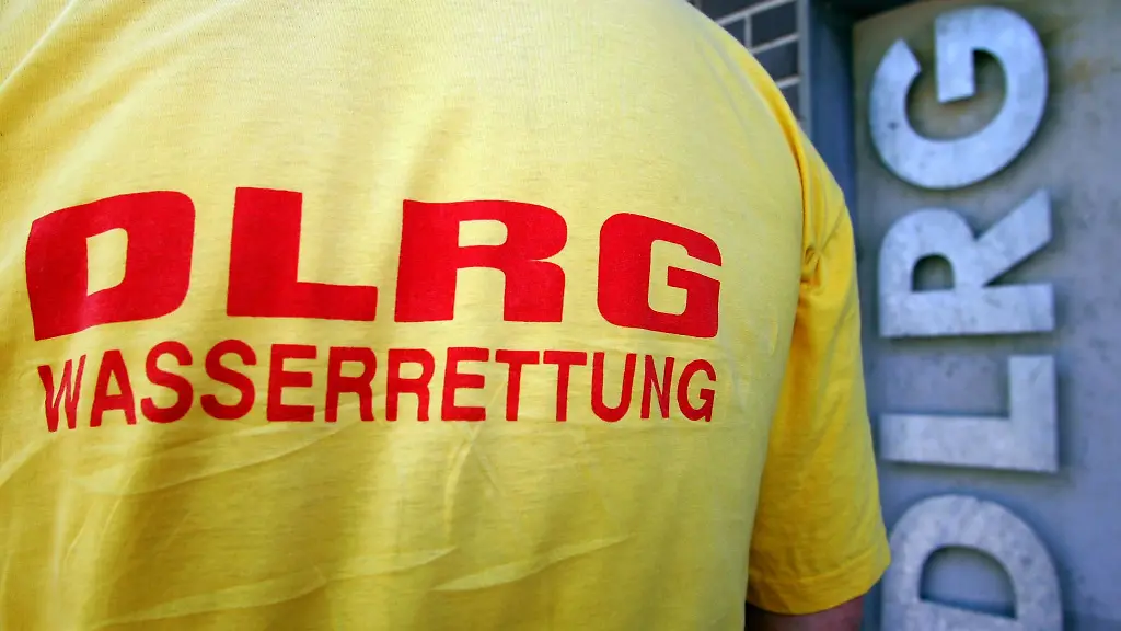 Ein-Helfer-der-DLRG-Deutsche-Lebens-Rettungs-Gesellschaft-steht-vor-einem-Logo