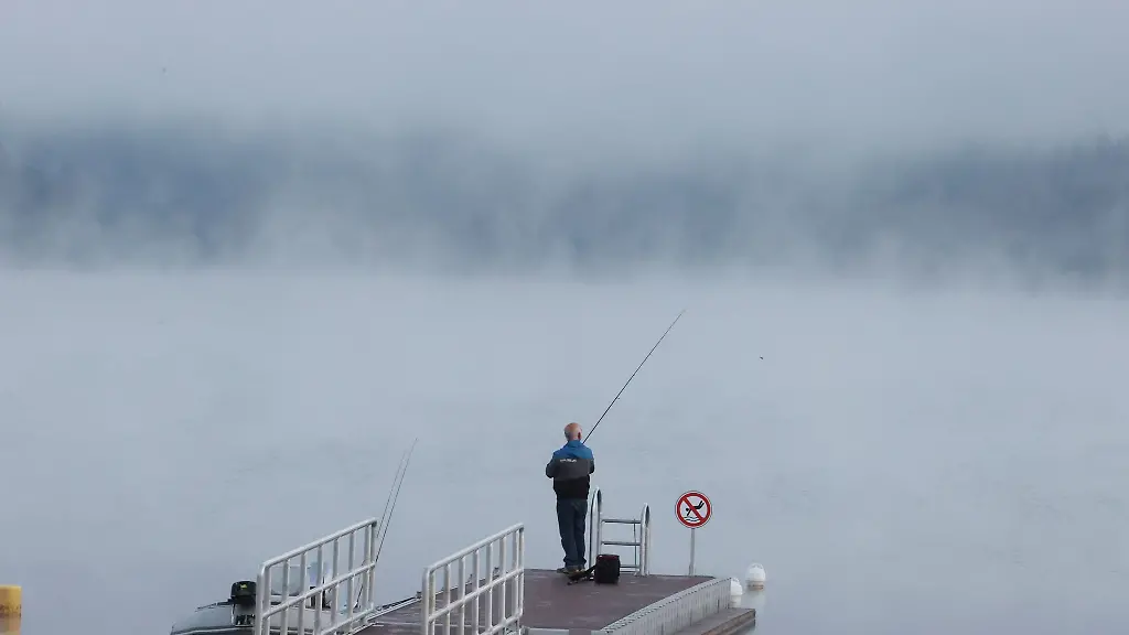Ein-Angler-steht-auf-einem-Steg-am-Ufer-der-Bleilochtalsperre-in-der-Morgendaemmerung