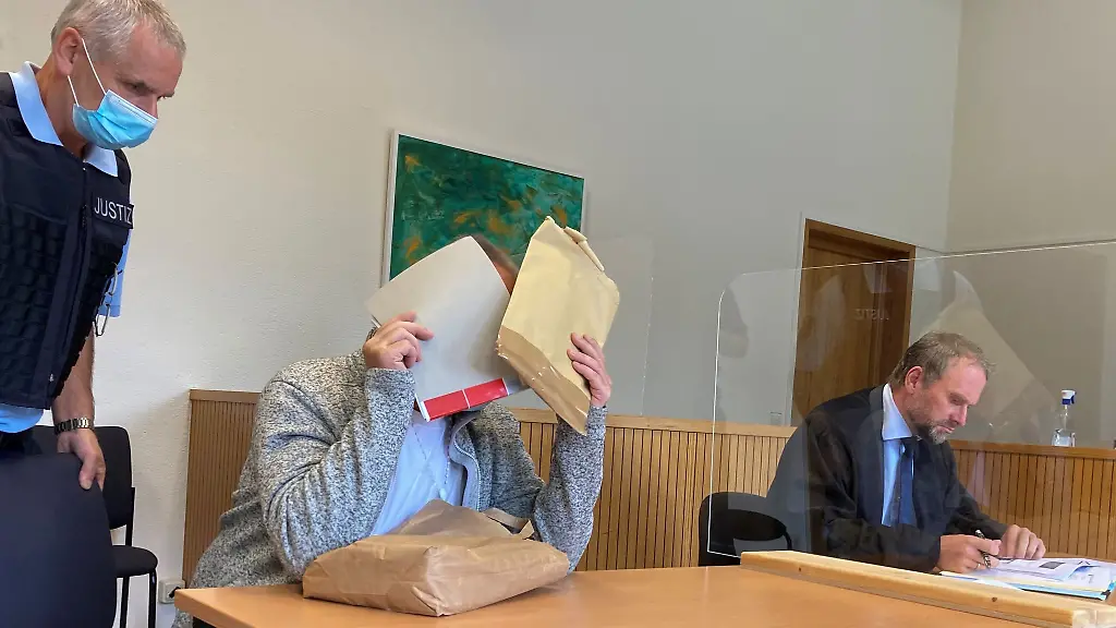 Der-Angeklagte-sitzt-im-Gerichtssaal-des-Amtsgerichts-und-haelt-sich-Akten-vor-sein-Gesicht