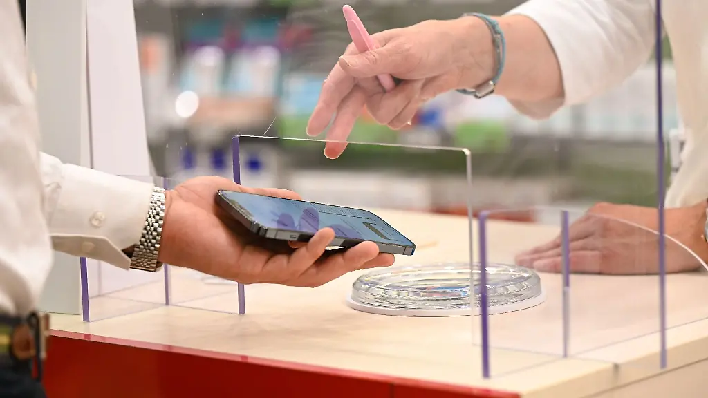 Ein-Mann-mit-seinem-Handy-in-der-Hand-wird-in-einer-Apotheke-von-einer-Apothekerin-bedient