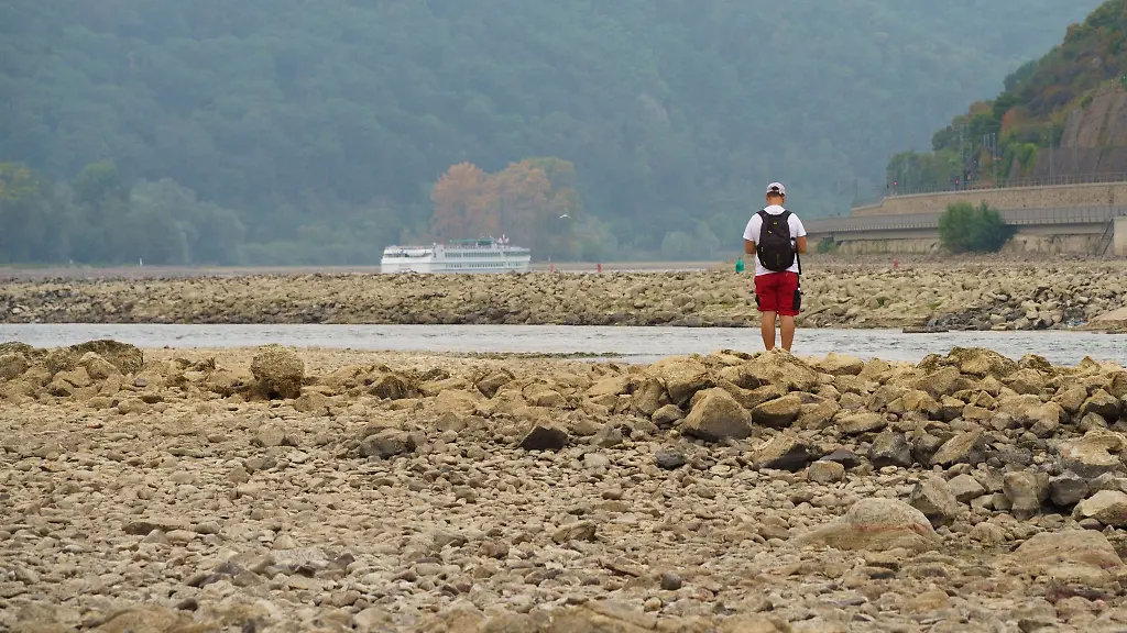 Ein-Mann-steht-auf-dem-Gestein-des-weitgehend-ausgetrockneten-Flussbetts-des-Rheins