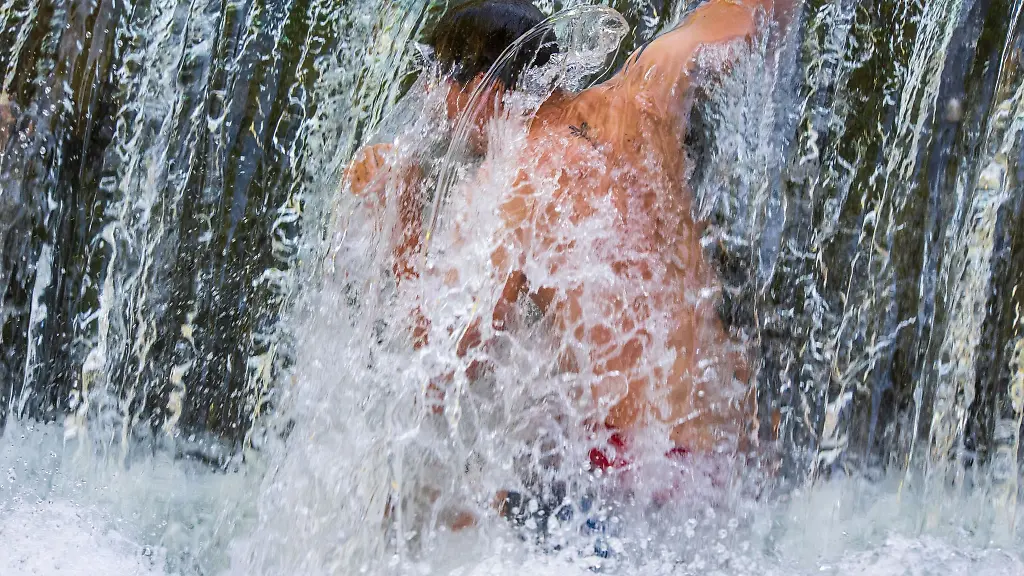 Ein-junger-Man-kuehlt-sich-unter-einem-kuenstlichen-Wasserfall-des-Eisbach-im-Englischen-Garten-ab