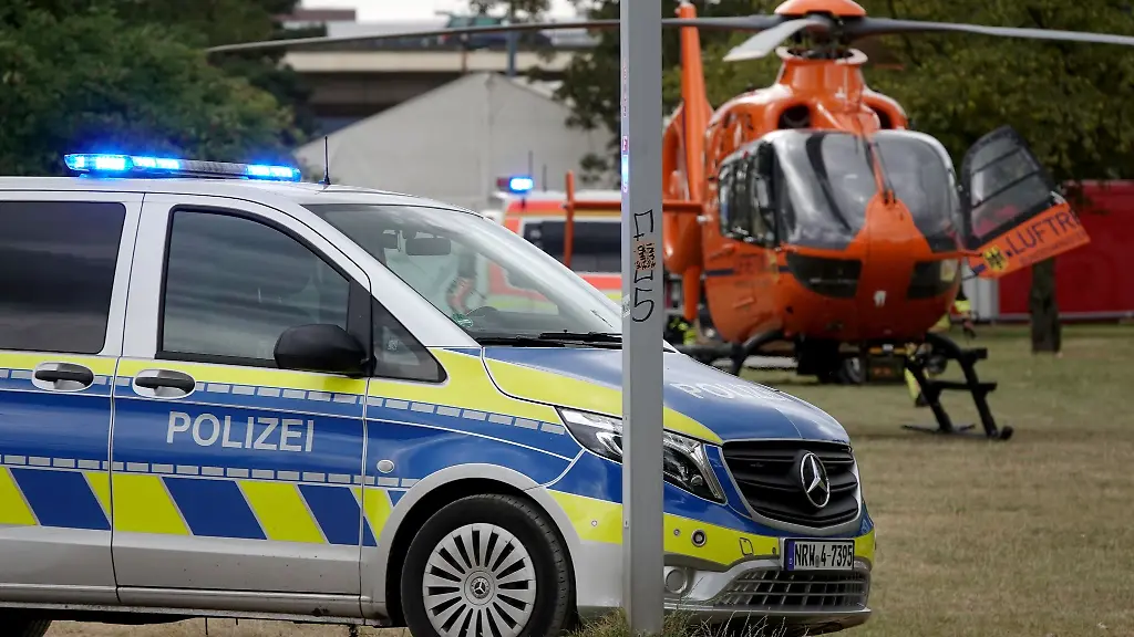 Ein-Rettungshubschrauber-und-ein-Polizeiauto-stehen-auf-den-Rheinwiesen