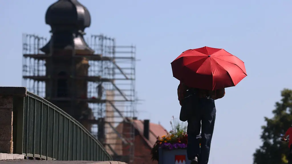 Ein-Mann-geht-mit-einem-roten-Sonnenschirm-ueber-die-Alte-Mainbruecke