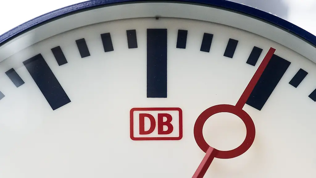 Eine-Uhr-mit-dem-Logo-der-Deutschen-Bahn-haengt-in-einem-Bahnhof