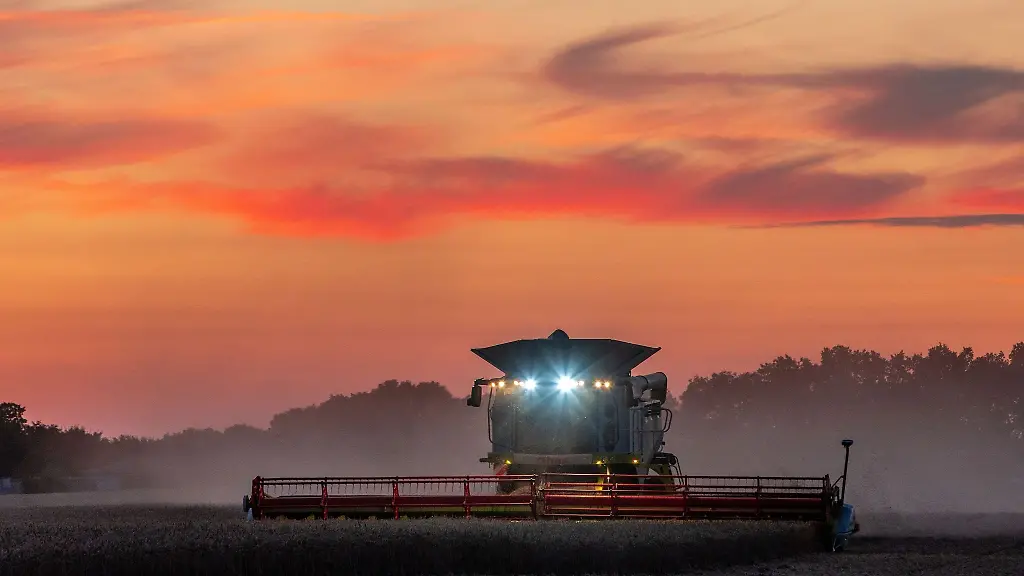 Ein-Maehdrescher-faehrt-nach-Sonnenuntergang-ueber-ein-Feld