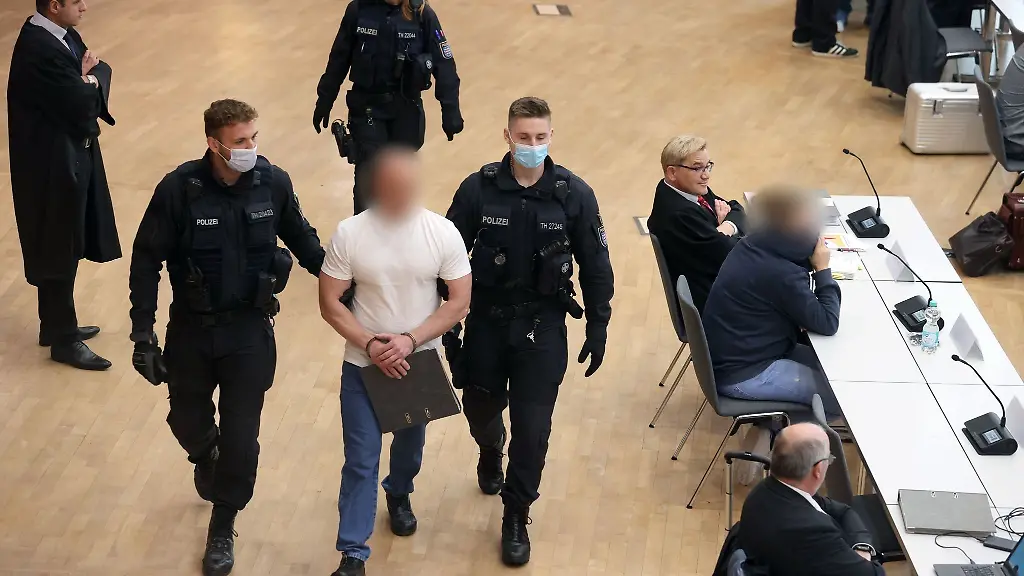 Ein-Angeklagter-M-wird-in-den-Verhandlungssaal-eine-weitere-Angeklagte-r-sitzt-bereits-an-ihrem-Platz