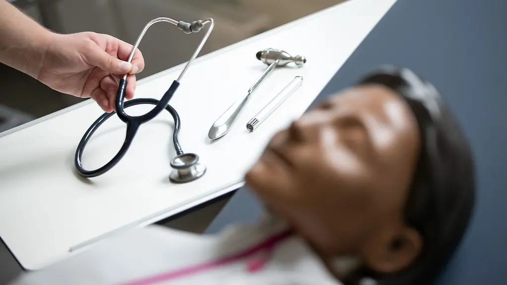 Ein-Mann-legt-in-einem-Raum-einer-Medizinischen-Fakultaet-ein-Stethoskop-neben-eine-Reanimationspuppe