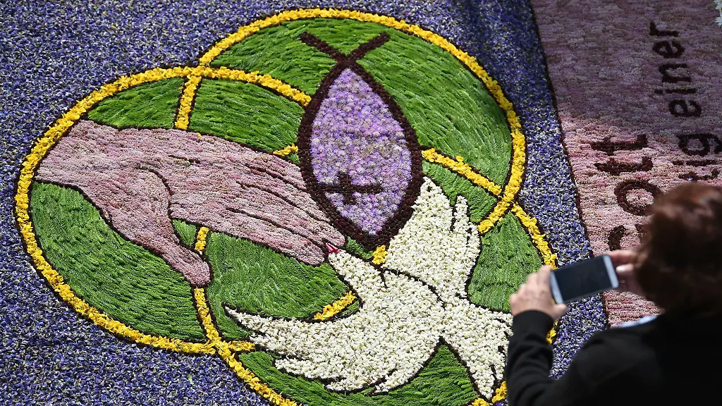 Eine-Frau-fotografiert-an-Fronleichnam-waehrend-der-Prozession-Kirchenmotive-in-einem-Blumenteppich