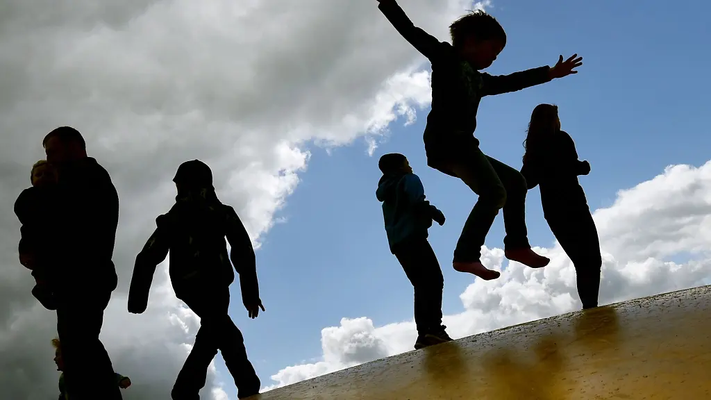Kinder-springen-auf-einer-Huepfburg-und-heben-sich-dabei-als-Schatten-vom-Himmel-ab