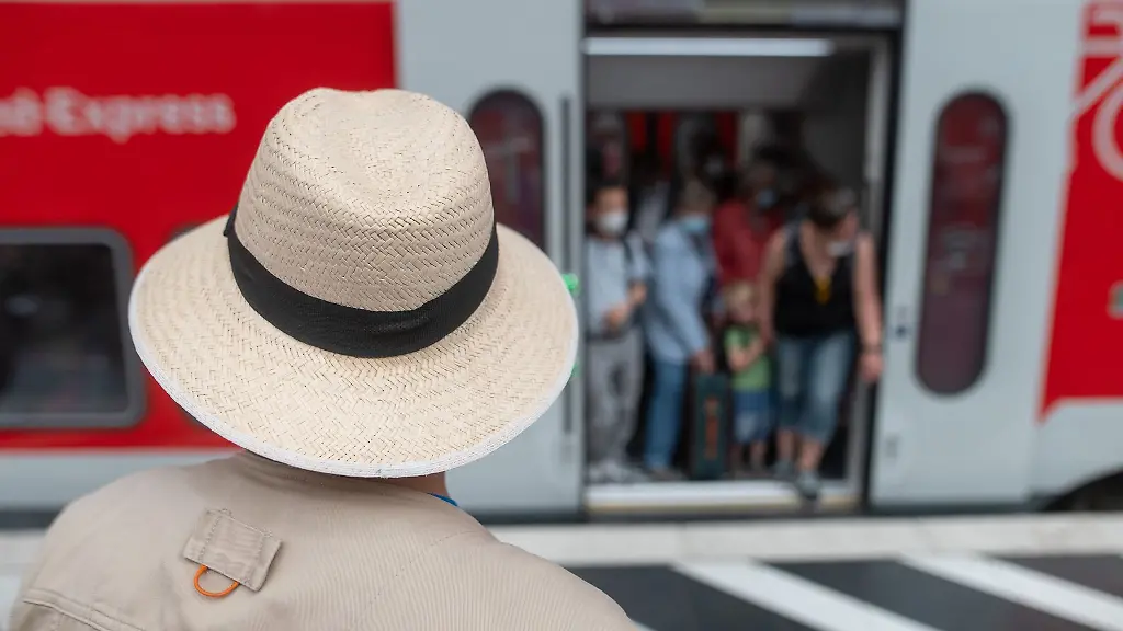 Ein-Mann-mit-Sonnenhut-steht-am-Hauptbahnhof-vor-dem-Pfingstwochenende-vor-einer-vollen-Regionalbahn