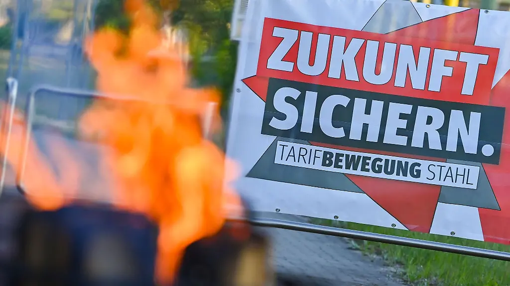 Ein-Feuer-brennt-neben-einem-Transparent-mit-der-Aufschrift-Zukunft-Sichern-Tarifbewegung-Stahl
