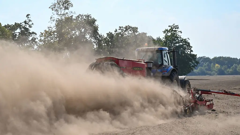 Ein-Landwirt-faehrt-mit-einem-Traktor-und-angehaengter-Drille-ueber-ein-Feld
