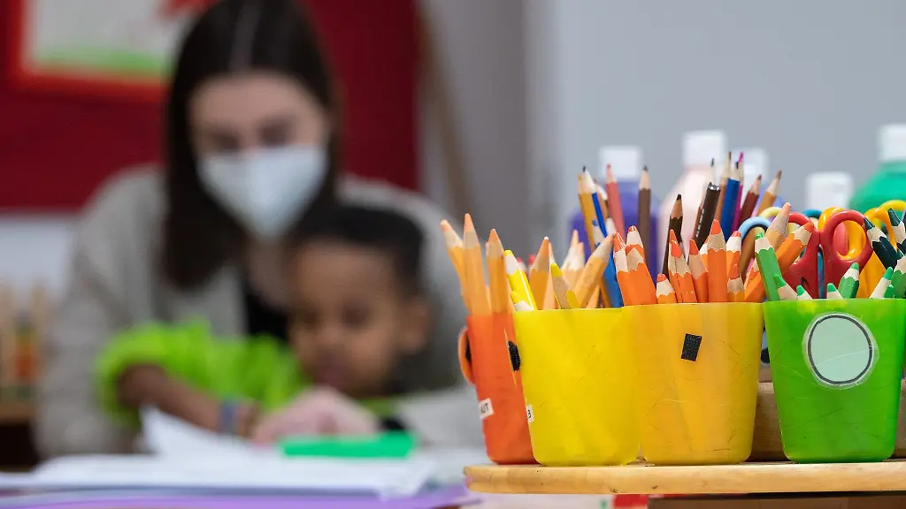 Eine-Erzieherin-sitzt-mit-einem-Kind-in-einer-Kita-hinter-Bechern-mit-Buntstiften