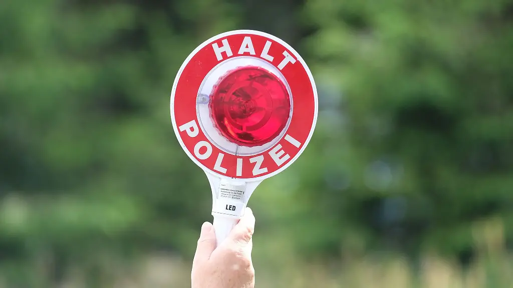 Eine-Polizistin-haelt-waehrend-einer-Polizeikontrolle-eine-rote-Winkerkelle-in-die-Hoehe