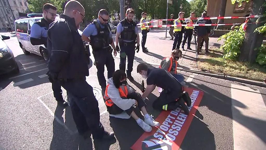 Aktivisten-haben-sich-auf-der-Strasse-fest-geklebt-und-ein-Polizist-versucht-den-Kleber-zu-loesen