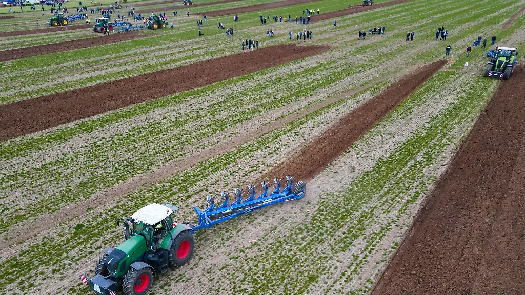 Traktoren-ziehen-unter-den-kritischen-Blicken-von-Schiedsrichtern-die-Pfluege-ueber-den-Acker