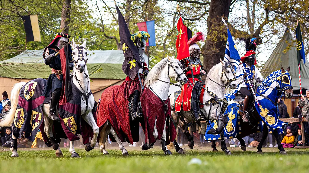 Akteure-in-Ritter-Optik-reiten-bei-dem-Ritterturnier-auf-Pferden-an-den-Zuschauern-vorbei