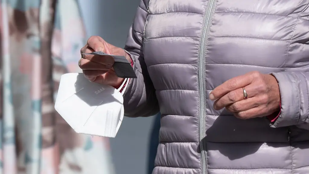 Eine-Frau-traegt-auf-einer-Einkaufsstrasse-eine-FFP-2-Maske-am-Handgelenk