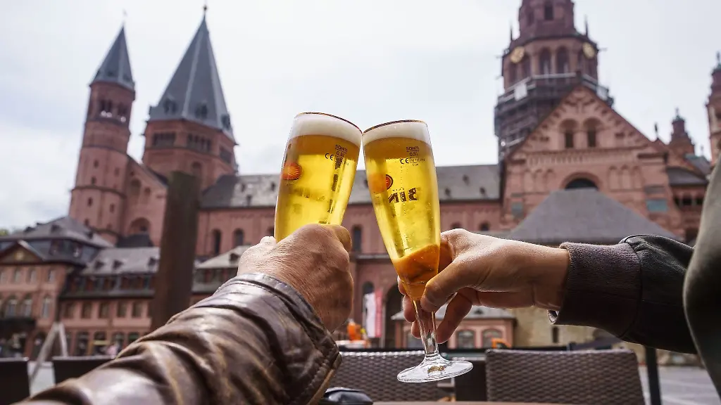 Zwei-Gaeste-stossen-auf-der-Terrasse-einer-Gaststaette-mit-einem-Bier-an