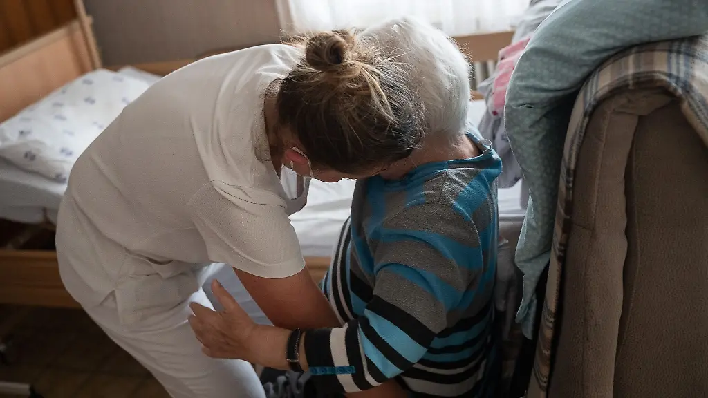 Eine-Pflegefachkraft-hilft-in-der-ambulanten-Pflege-einer-Frau-beim-Umsetzen