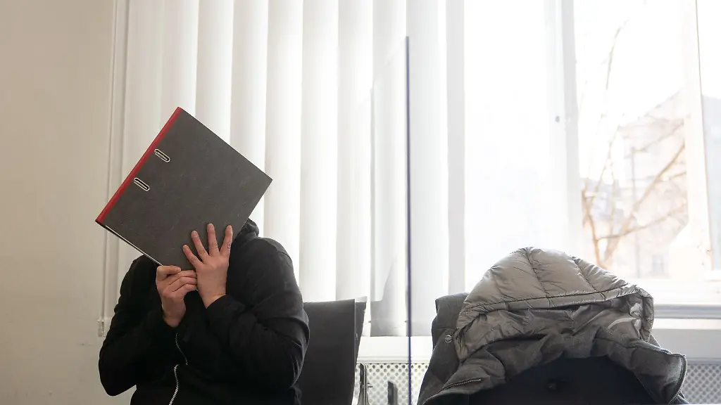 Die-Angeklagte-haelt-sich-im-Gerichtssaal-einen-Ordner-vor-ihr-Gesicht