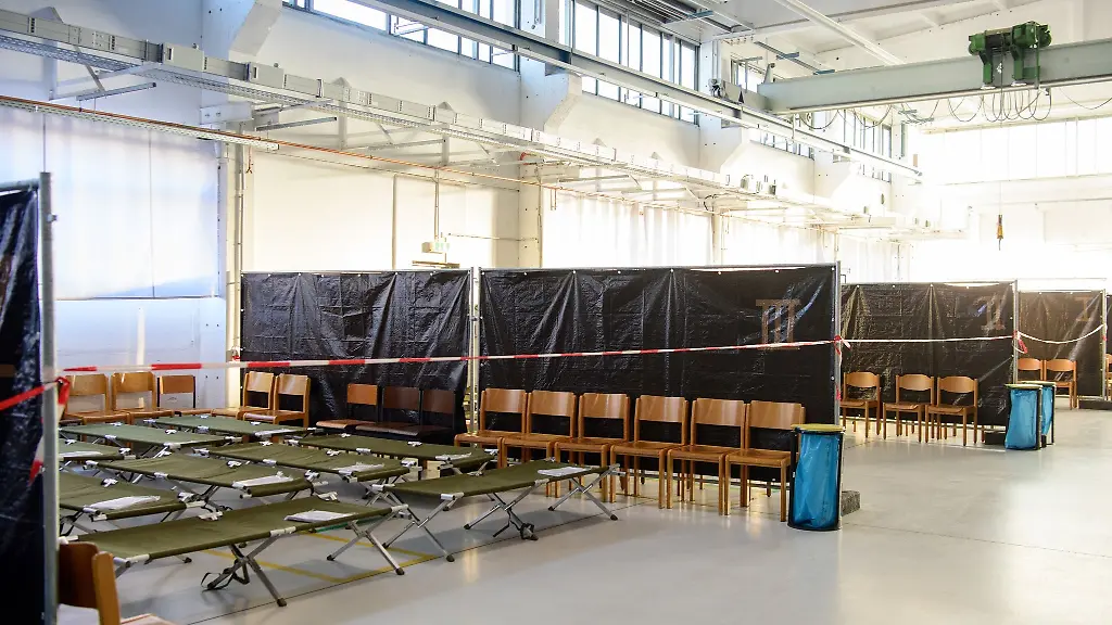 Feldbetten-und-Holzstuehle-stehen-in-einer-Halle-der-Zentralen-Bearbeitungsstrasse-der-Bundespolizei-in-Markendorf-hinter-einem-rot-weissen-Absperrband