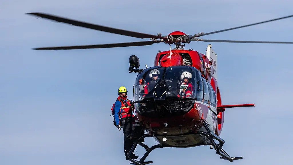 Ein-Mitglied-der-Bergwacht-steht-auf-den-Kufen-eines-Rettungshubschraubers