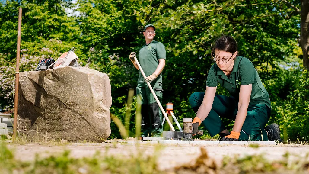 Zwei-Gartenbauer-beim-Befestigen-eines-Weges-in-einer-Gartenanlage