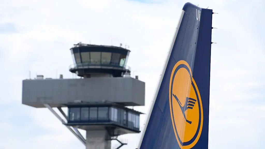 Das-Logo-am-Leitwerk-einer-Lufthansa-Maschine-ist-vor-der-Kulisse-eines-Towers-zu-sehen