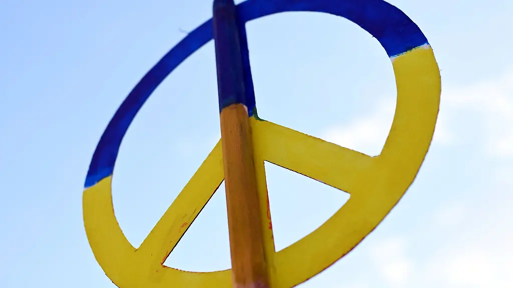 Bei-einer-Mahnwache-zum-Ukraine-Krieg-wird-ein-Friedenssymbol-in-den-Farben-der-Ukraine-in-den-Himmel-gehalten