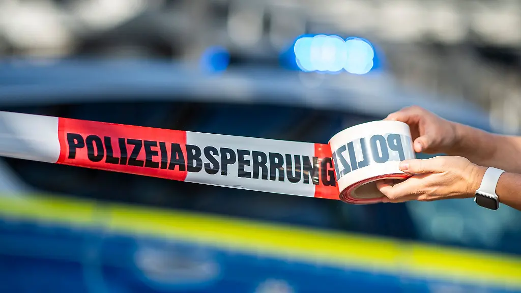 Ein-Absperrband-wird-vor-einem-Polizeiwagen-ausgerollt