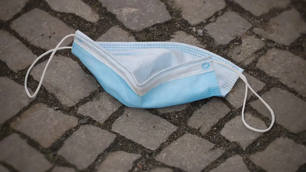 Eine-Schutzmaske-fuer-Mund-und-Nase-liegt-in-der-Stadt-auf-einem-Fussweg