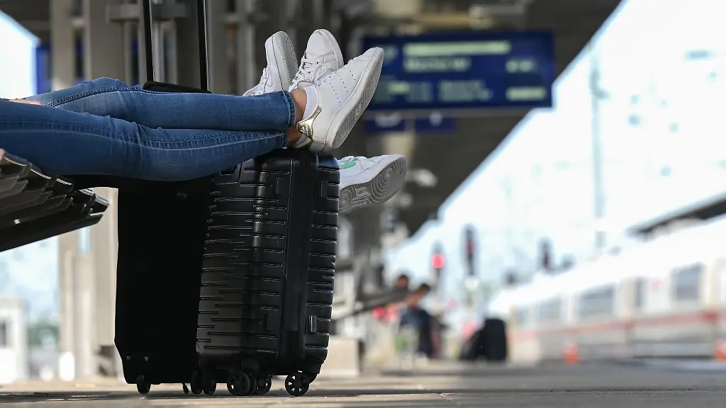 Zwei-Reisegaeste-warten-an-einem-Bahnhof-am-Gleis