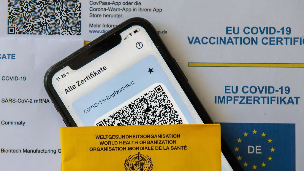 Ein-Impfpass-und-ein-Smartphone-mit-der-CovPass-App-liegen-auf-einem-Impfzertifikat