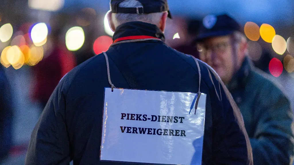 Ein-Teilnehmer-der-Protestaktion-gegen-die-Corona-Schutzmassnahmen-traegt-ein-Schild-mit-der-Aufschrift-Pieks-Dienst-Verweigerer