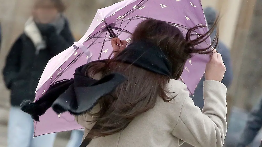 Eine-Passantin-mit-wehenden-Haaren-sichert-ihren-Regenschirm